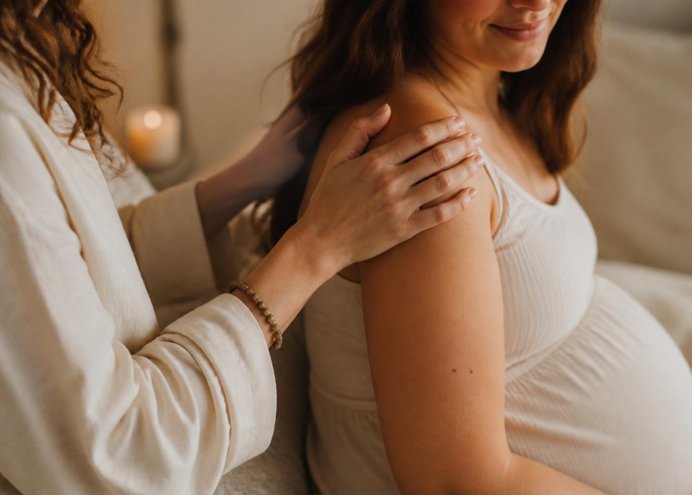 A doula's hand resting gently on the shoulder of a pregnant woman